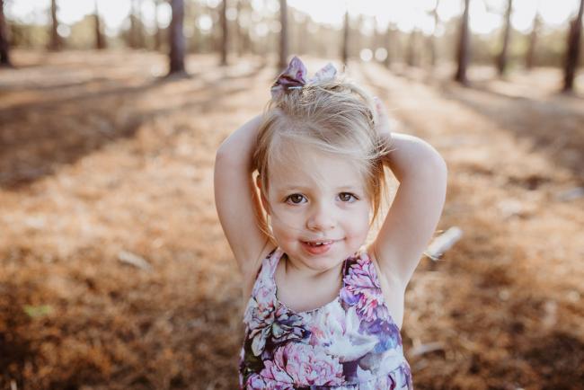 Little girl with arms behind her head and smiling at the camera during an extended family photography session at The Pines Wanneroo in Perth