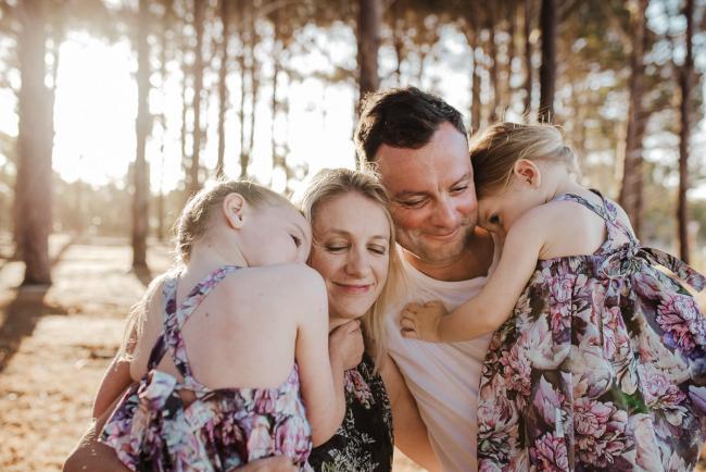 Family of four cuddling with their eyes closed during an extended family photography session at The Pines Wanneroo in Perth