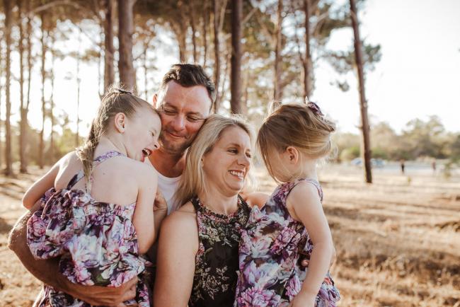 Family of four cuddling and smiling at each other during an extended family photography session at The Pines Wanneroo in Perth