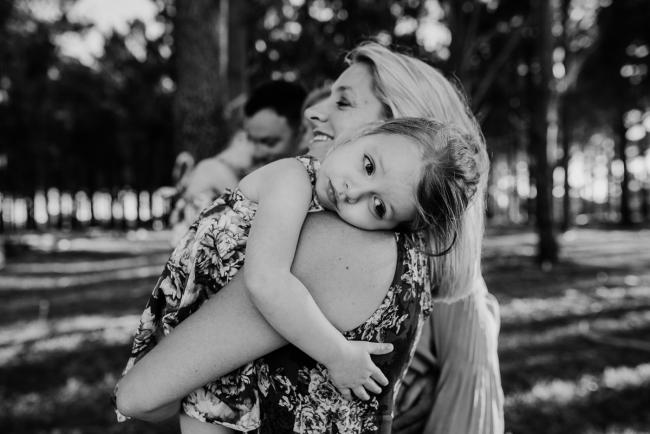 Black and white image of little girl cuddling over her mums shoulder during an extended family photography session at The Pines Wanneroo in Perth