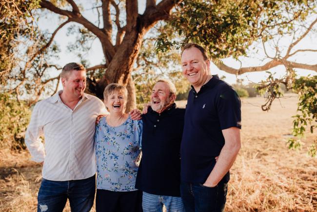Parents with their two grown sons arm in arm and laughing during an extended family photography session at Perry's Paddock in Perth