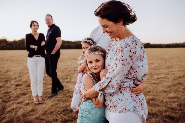 Mother and daughter hugging with others in the background during an extended family photography session at Perry's Paddock in Perth