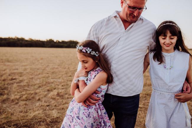 Little girl with her fathers arms wrapped around her during an extended family photography session at Perry's Paddock in Perth