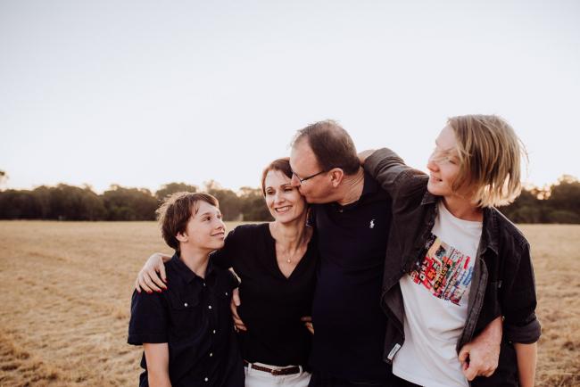 Family of 4 with the father kissing the mother during an extended family photography session at Perry's Paddock in Perth