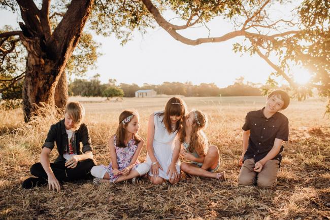 Cousins sitting under a tree playing Chinese Whispers during an extended family photography session at Perry's Paddock in Perth