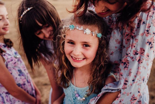 Little girl smiling up at the camera while her mother and sister smile down at her during an extended family photography session at Perry's Paddock in Perth