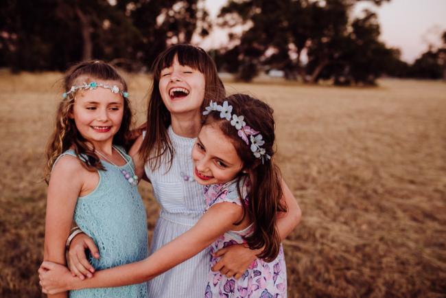 Three sisters hugging and laughing during an extended family photography session at Perry's Paddock in Perth