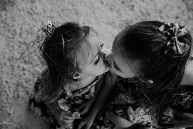 Black and white top down image of sisters kissing during an extended family photography session at The Pines Wanneroo in Perth