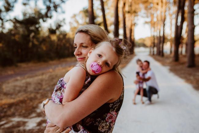 Daughter cuddling her mother with a dummy in her mouth during an extended family photography session at The Pines Wanneroo in Perth