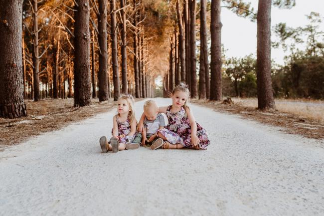 Two girls and a boy sitting on the ground during an extended family photography session at The Pines Wanneroo in Perth