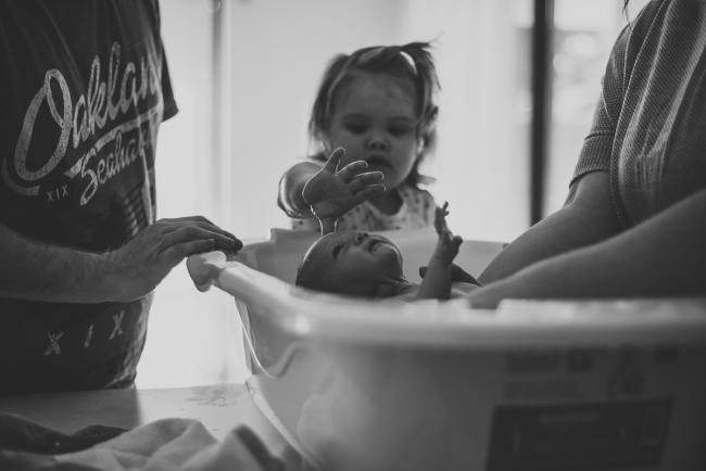 20180720-DSC_8700-1 Black and white image of a new baby being bathed by her parents and big sister during a newborn lifestyle session in Perth