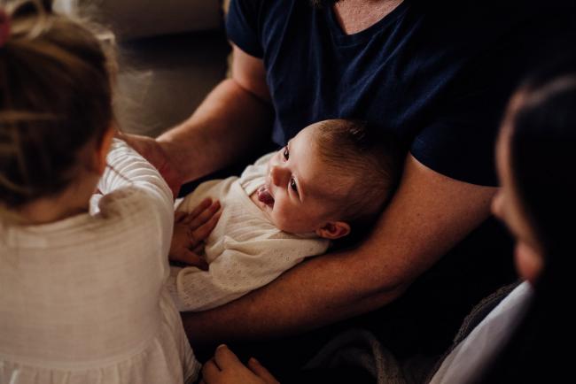 20180725-DSC_1408 New baby cradled in her dad's arms and smiling at her big sister during a newborn lifestyle session in Perth