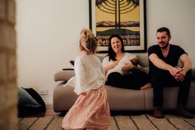 newborn_lifestyle_photographer_perth Little girl dancing in her living room in front of her parents and her new baby sister during their Perth newborn lifestyle session