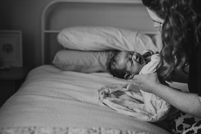 20180927-DSC_8182 Black and white image of a mother placing her crying baby on the bed during a lifestyle newborn photography session in Perth