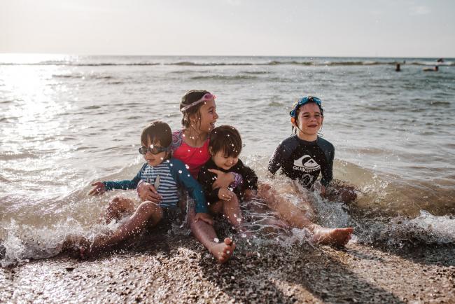 Four kids sitting in the water as a small wave hits them with Perth family photographer