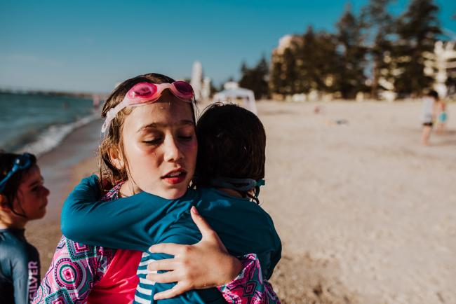 Little girl carrying her younger brother on the beach with Perth family photographer