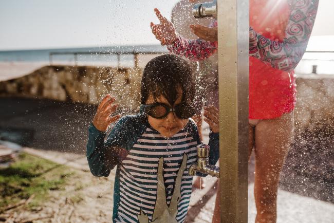 Little boy standing under water from the tap on the beach with Perth family photographer