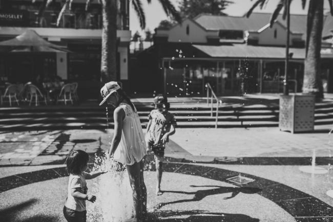 Black and white image of three kids playing in a water play area in Glenelg Adelaide with Perth family photographer