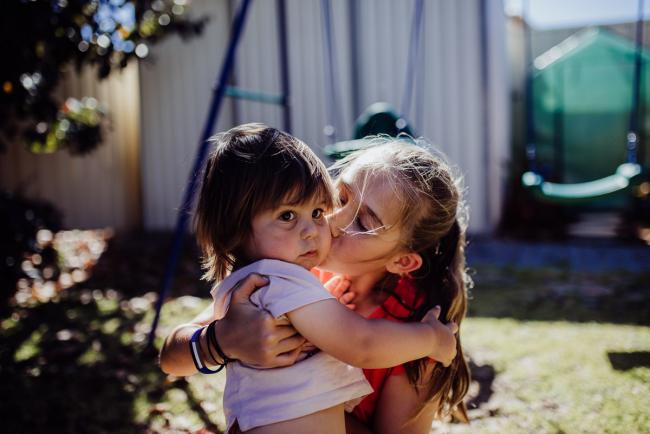 Older sister kissing her younger brother outside with Perth family photographer
