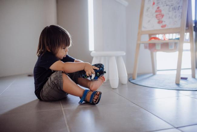 Little boy sitting on the floor trying to put shoes on with Perth family photographer