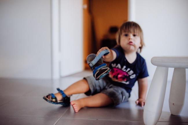 Little boy sitting on the floor and holding out his shoe to the camera with Perth family photographer