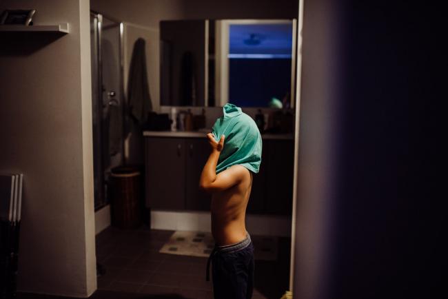 Little boy pulling his top over his head to get dressed with Perth family photographer