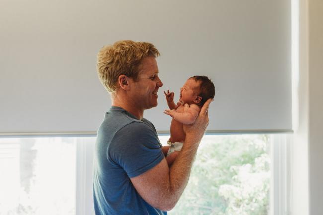 Dad holds baby up to his face in front of a window during a Perth Fresh 48 photography session