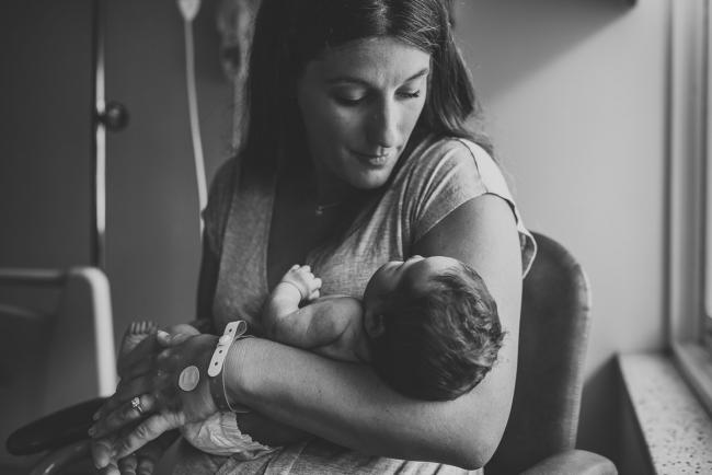 Black and white image of mum holding her new baby in her arms and looking down at her during Fresh 48 Photography Perth session
