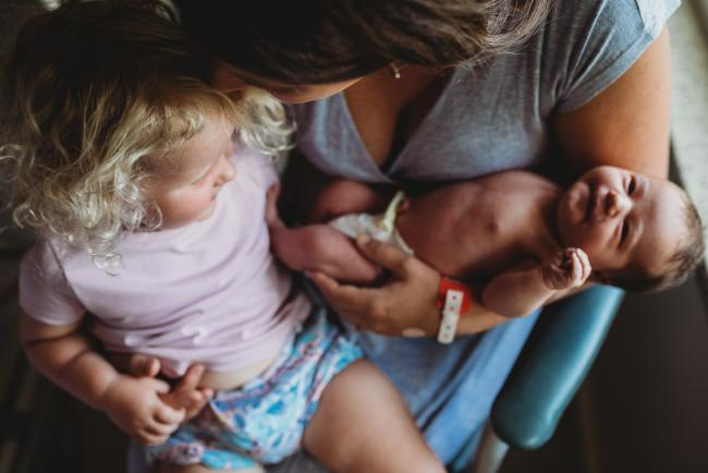 Mother holding her new baby and kissing her older daughter during a Perth Fresh 48 photography session