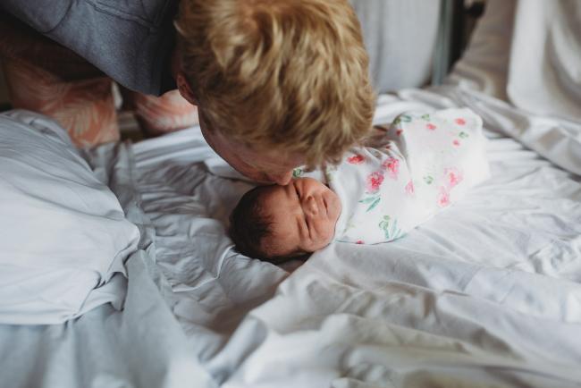Father leaning over and kissing his new baby who is laying wrapped on the hospital bed during Fresh 48 Photography Perth session
