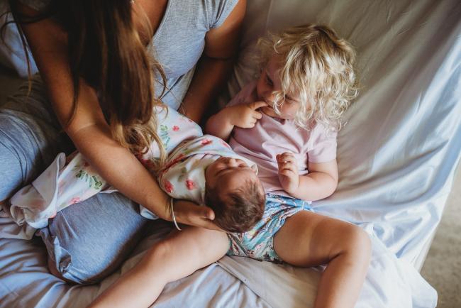 Mother holds new baby on the lap of her big sister during a Perth Fresh 48 photography session