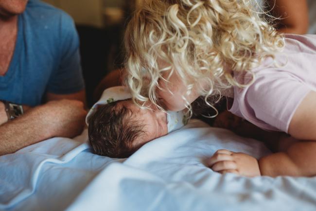 Big sister leans over and kisses her new baby sister during a Perth Fresh 48 photography session