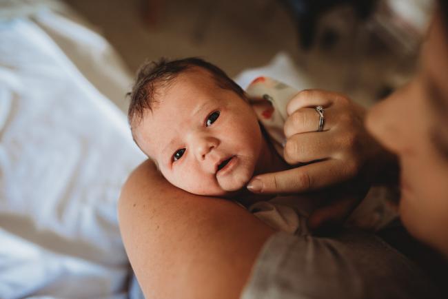 Close up of new baby looking up at the camera whilst in her mothers arms during Fresh 48 Photography Perth session