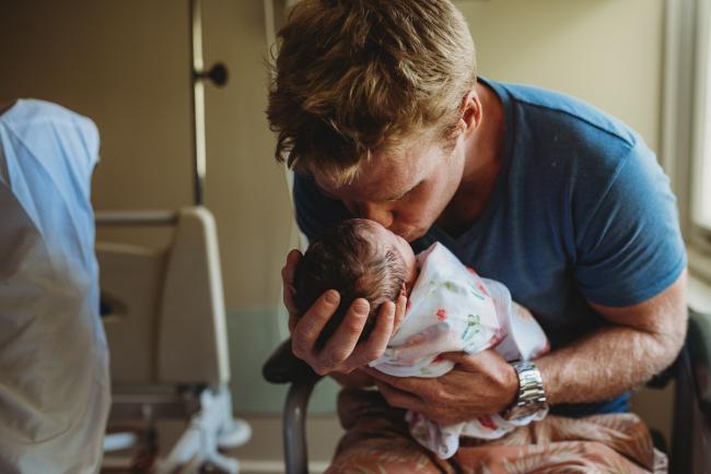 Father holds new baby and kisses her during a Perth Fresh 48 photography session