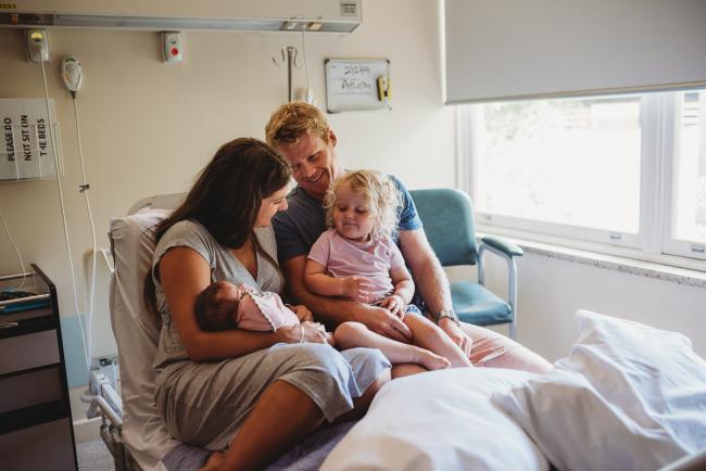 New family of 4 sit on a hospital bed with their new baby during a Perth Fresh 48 photography session