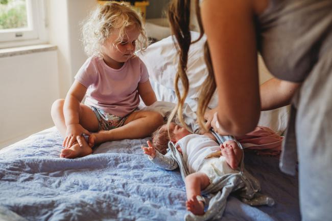Mother changing her new baby on the hospital bed whilst big sister looks on during Fresh 48 Photography Perth session