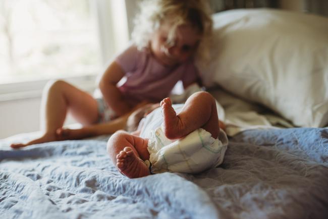 New baby's feet with big sister sitting and looking at her during Fresh 48 Photography Perth session