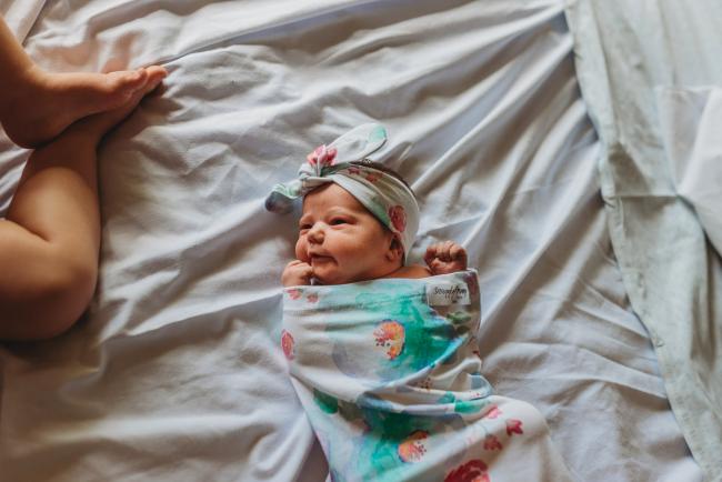New baby lays wrapped on a bed with big sisters feet in the frame during a Perth Fresh 48 photography session