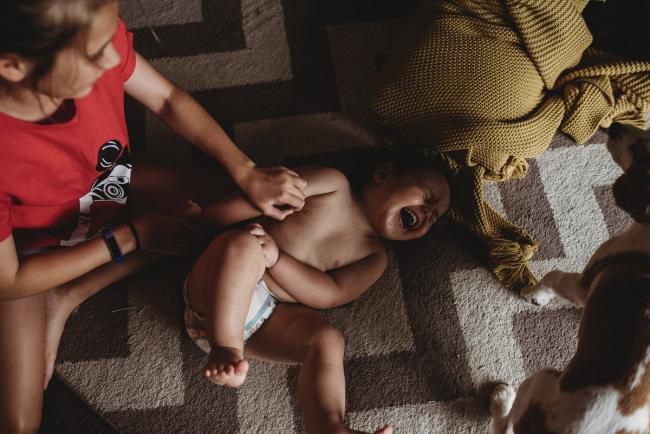 Little boy in a nappy being tickled on the ground by his older sister with Perth family photographer