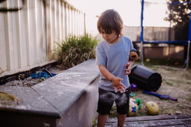 Little boy throwing sand off a bench outside with Perth family photographer