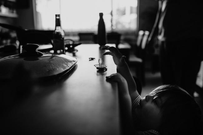 Black and white image of little boy reaching onto the bench to get his dummy by Perth family photographer