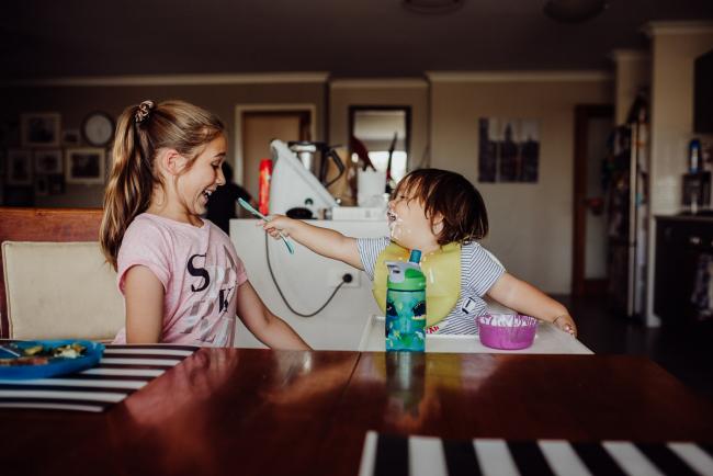 Little boy trying to feed his big sister at the dinner table with Perth family photographer