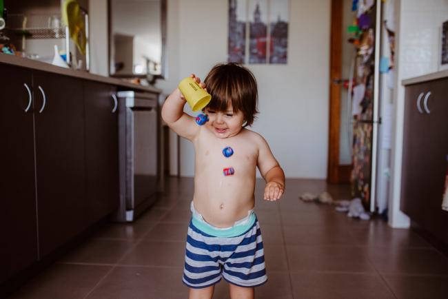 Little boy throwing dice out of a cup in the kitchen with Perth family photographer