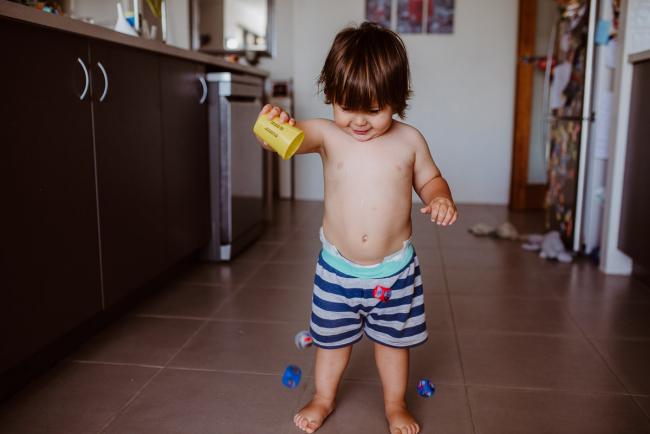 Little boy throwing dice out of a cup in the kitchen with Perth family photographer