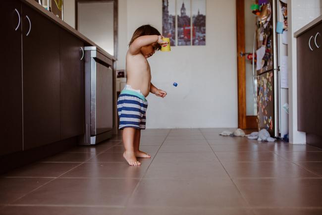 Little boy throwing dice out of a cup in the kitchen with Perth family photographer