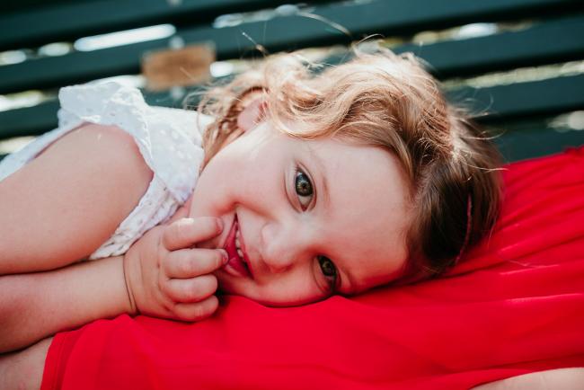 Family-Photographer-Perth-Hyde-Park-12-of-34 Little girl laying on her big sisters lap and smiling at the camera during a Perth family photography session at Hyde Park