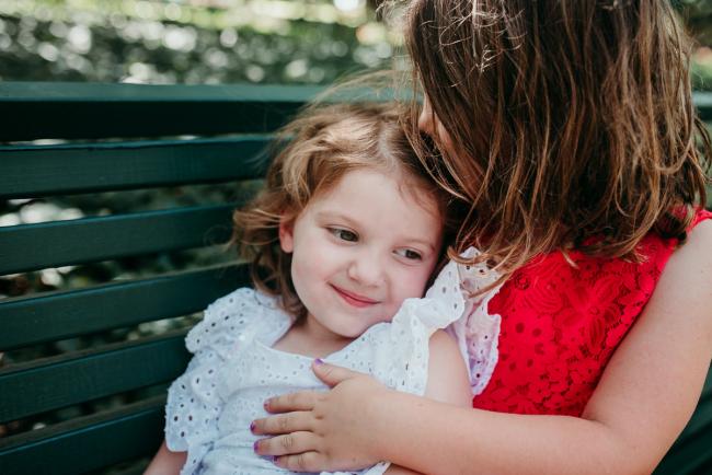Family-Photographer-Perth-Hyde-Park-13-of-34 Two sisters hugging on a park bench during a Perth family photography session at Hyde Park