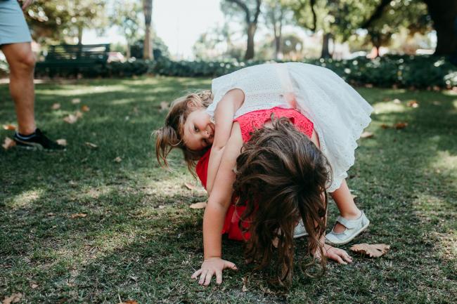 Family-Photographer-Perth-Hyde-Park-17-of-34 Little girl laying across her sisters back during a Perth family photography session at Hyde Park