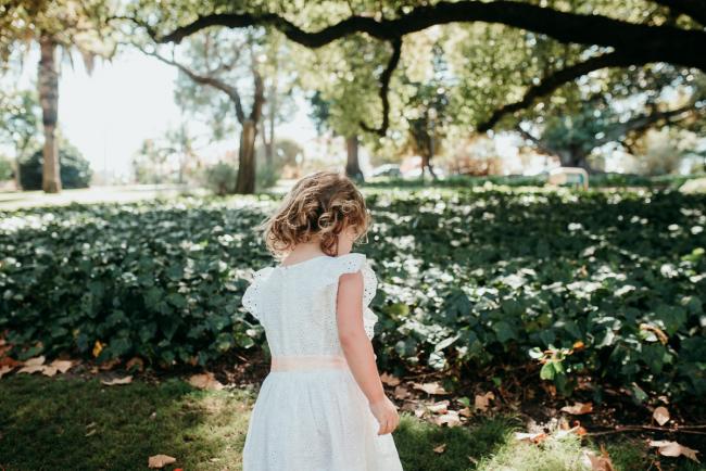 Family-Photographer-Perth-Hyde-Park-29-of-34 Back of little girl in a white dress as she faces the garden during a Perth family photography session at Hyde Park