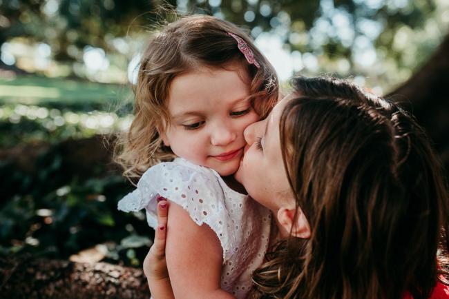 Two sisters kissing during a Perth family photography session at Hyde Park